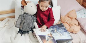 a little girl reads on her bed with a stuffed animal