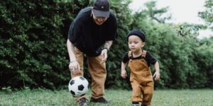 a toddler learns to play soccer with his dad