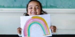 a girl holds up a painting of a rainbow