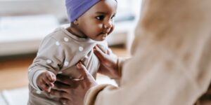 a parent supports a baby learning to walk